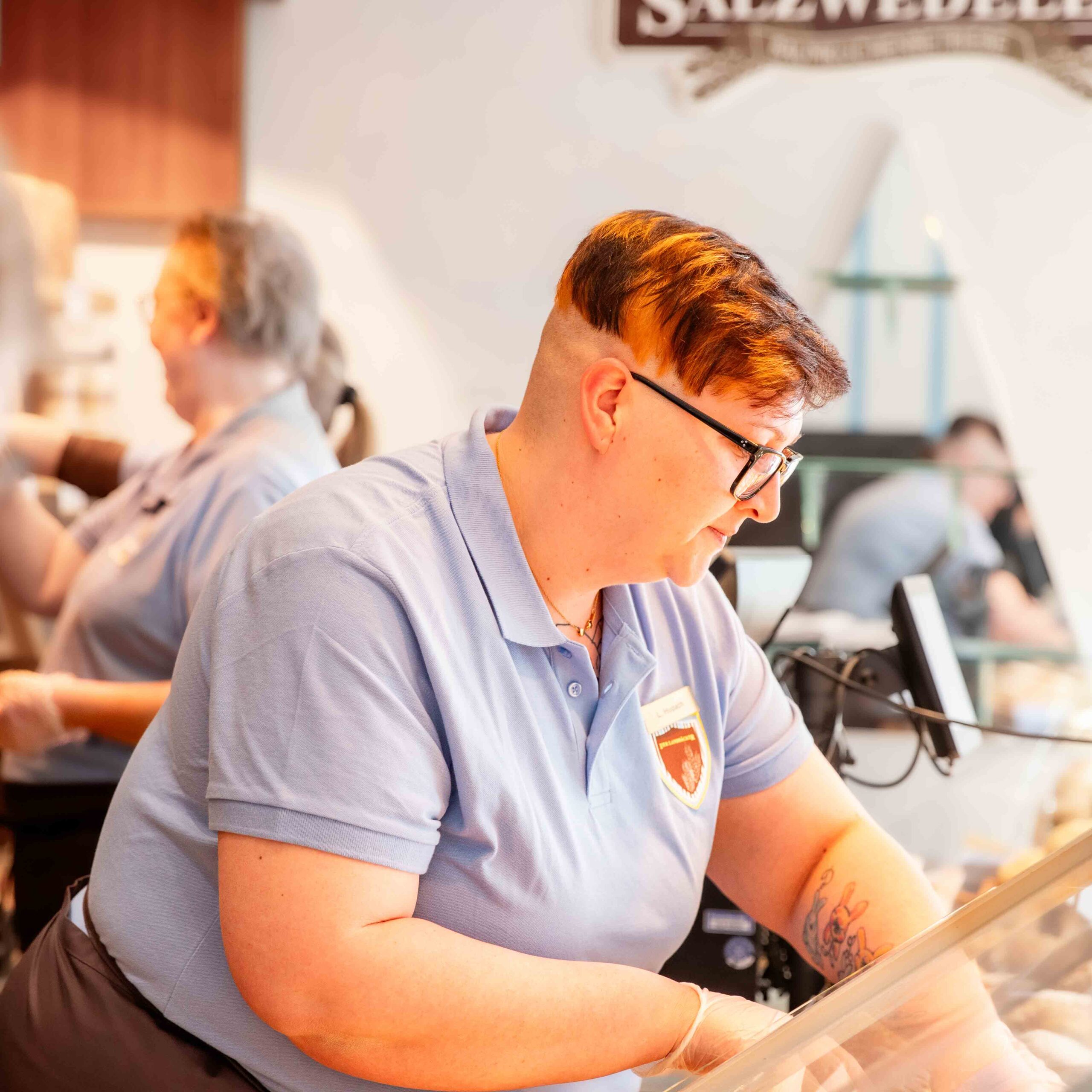 Bäckerei Fachverkäuferin, ca. 35 Jahre alt, sortiert konzentriert in Arbeitskleidung die Thekenauslage derBäckerei Filiale.