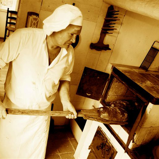 Bäcker und Gründer von Ihr Landbäcker Andreas Boss, in Traditioneller Bäckerkleidung in einer rustikalen Backstube holt Brote aus dem Ofen.