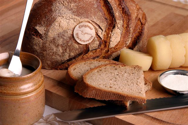 Brotlaib aufgeschnitten präsentiert mit Butter, Käse & Salz auf einem Holzbrett.