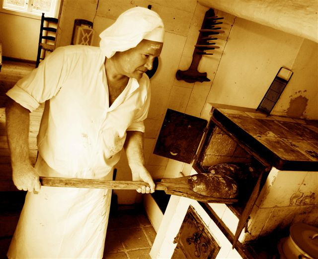 Bäcker und Gründer von Ihr Landbäcker Andreas Boss, in Traditioneller Bäckerkleidung in einer rustikalen Backstube holt Brote aus dem Ofen.