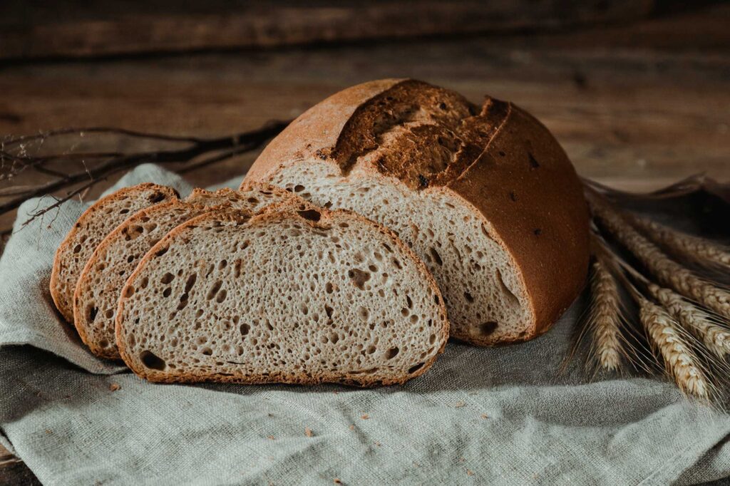Ein aufgeschnittener Brotlaib mit drei Brotscheiben mit Leinen-Tuch und Weizenähren arrangiert.